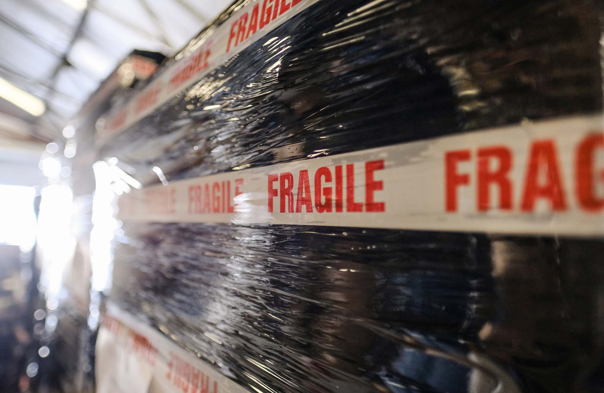 Shallow focus of a Fragile letter seen on generic packaging tape, seen stuck to a large delivery about to be shipped from a warehouse.